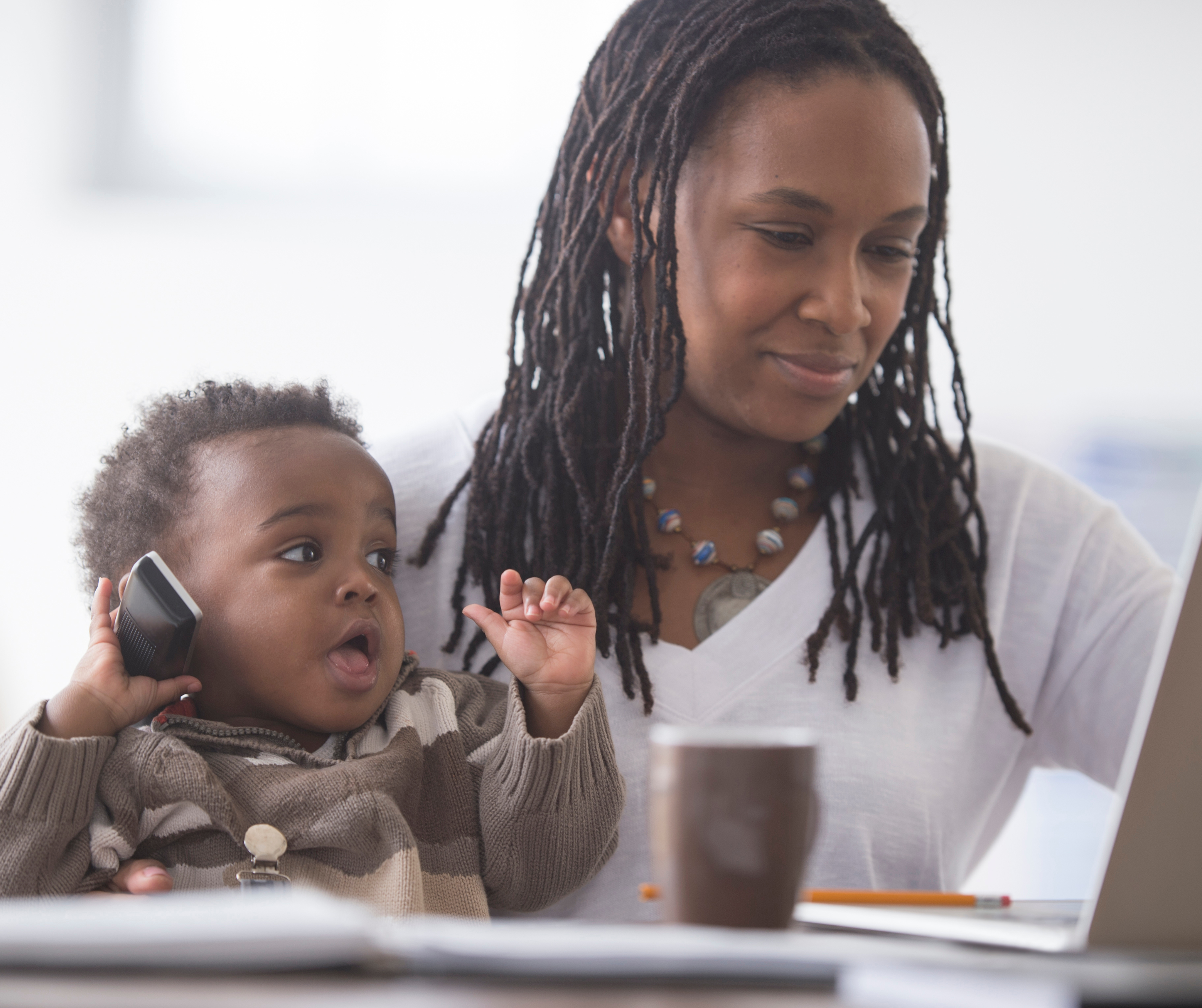 Batswana mother holding baby whilst working on laptop.