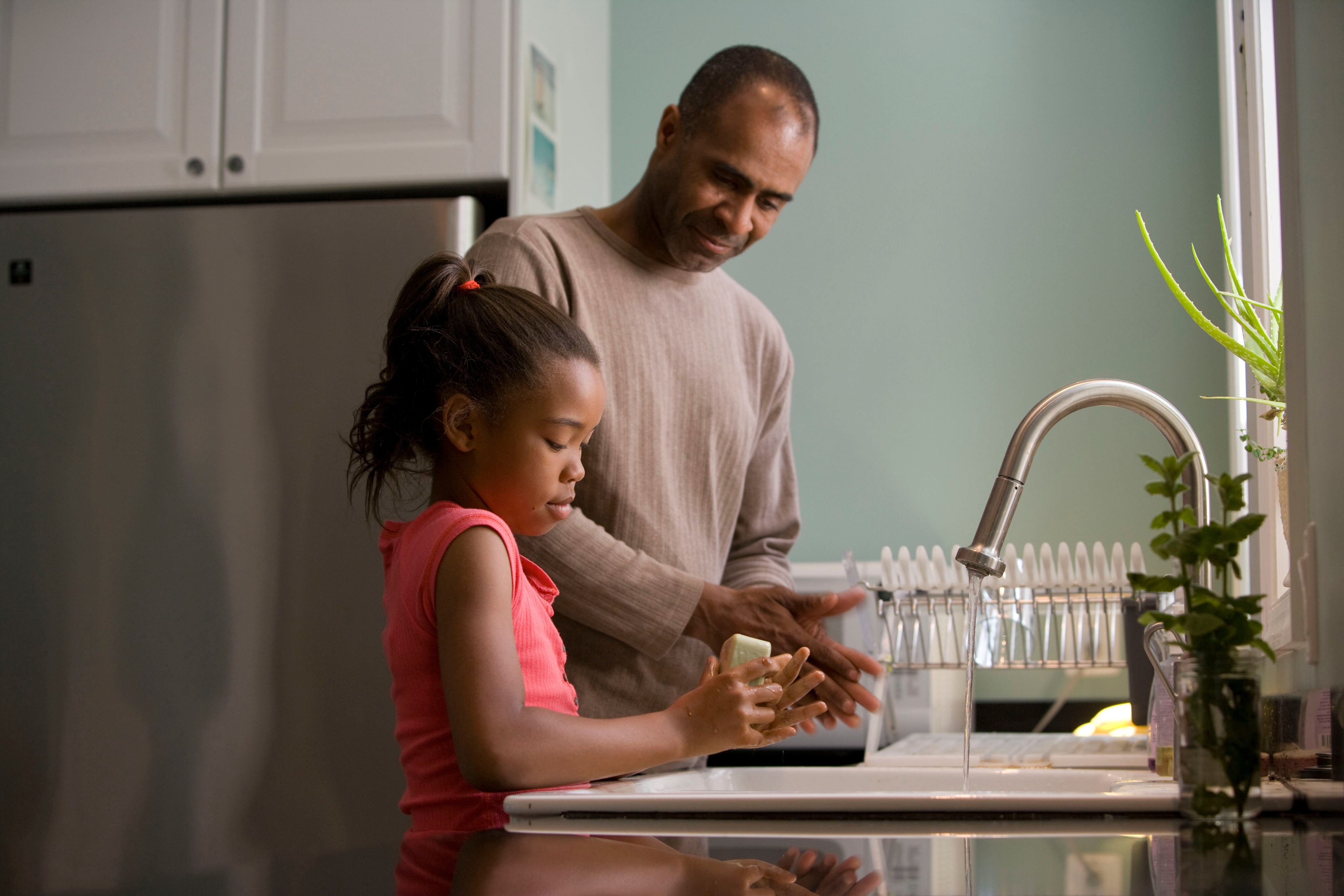 daughter washing hands at kitchen sink with father