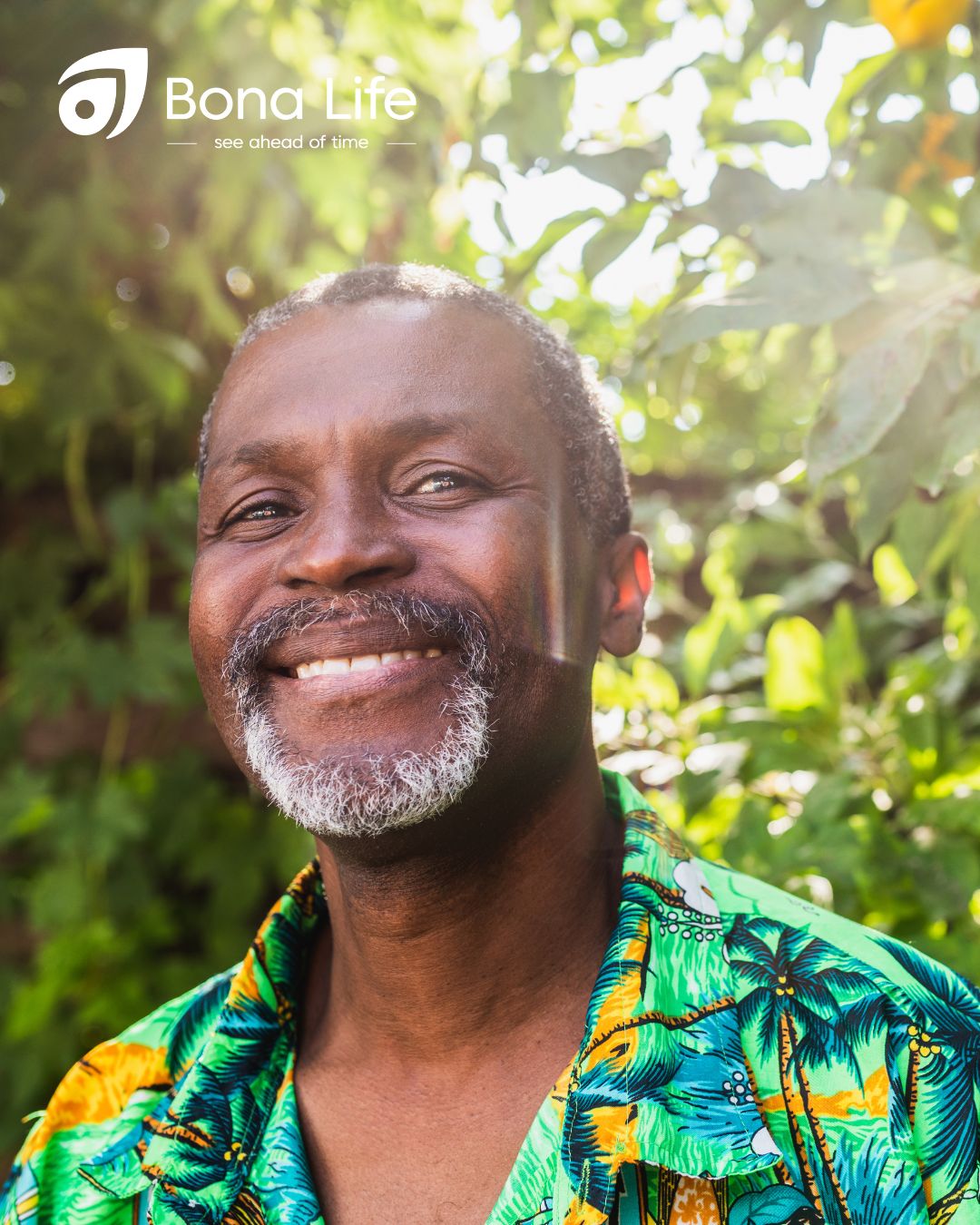 Man in floral shirt smiling under tree